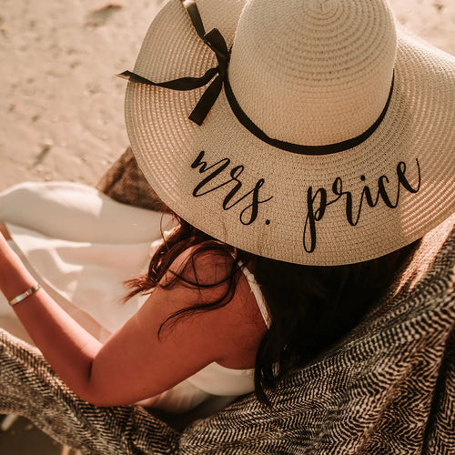 Bride wearing personalised floppy sun hat with black bow and custom embroidery by the beach